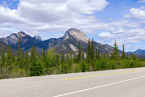 Empty highway among mountains and forests under the blue cloudy sky. Sunny summer day.