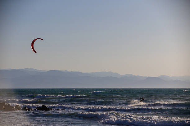 Athlete enjoying extreme kitesurfing on Cyprus coastline, flying over the blue sea with mountains in the distance under bright sunlight