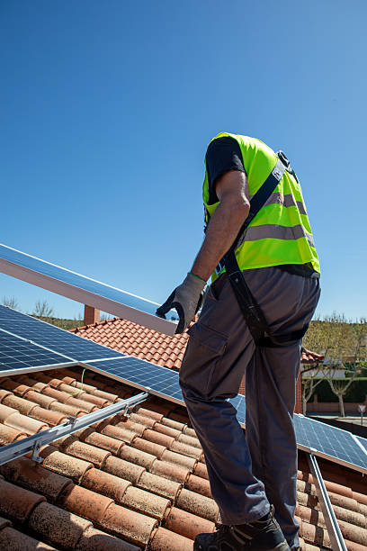 istock A worker in a reflective vest is on a rooftop, carefully installing solar panels. The sky is clear and blue, indicating a sunny day. The neighborhood is calm with clean rooftops. 2233257441