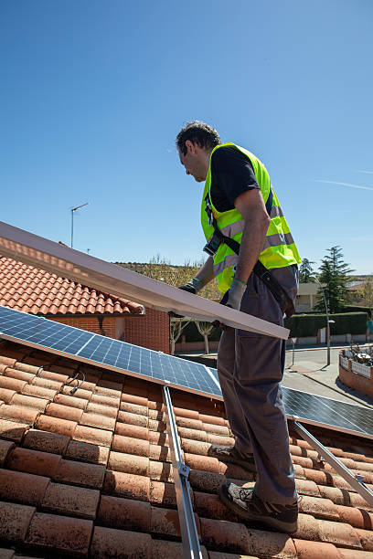 istock A worker in a reflective vest is on a rooftop, carefully installing solar panels. The sky is clear and blue, indicating a sunny day. The neighborhood is calm with clean rooftops. 2233257446