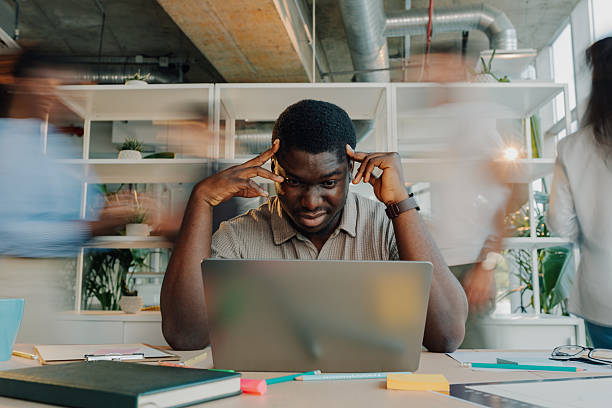 istock Stressed young man suffering headache working on laptop in busy office 2233257783