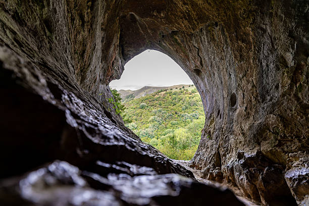istock Exploring natural rock cave overlooking green valley landscape 2233261323