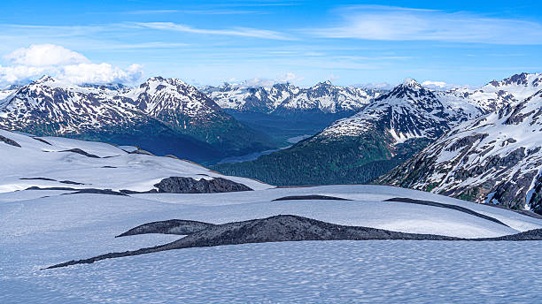 Snowy mountain majesty dominates the landscape of Alaska's Kenai Fjords National Park, located in the United States. The park offers breathtaking views of glaciers and rugged terrain under azure skies.