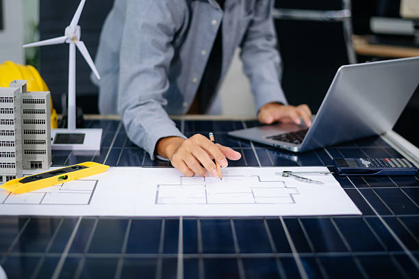 istock Architect planning eco-friendly building with wind turbine model, blueprints, and laptop. Ideal for green energy, smart city, 2233272019