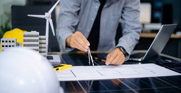 istock Architect planning eco-friendly building with wind turbine model, blueprints, and laptop. Ideal for green energy, smart city, 2233272020