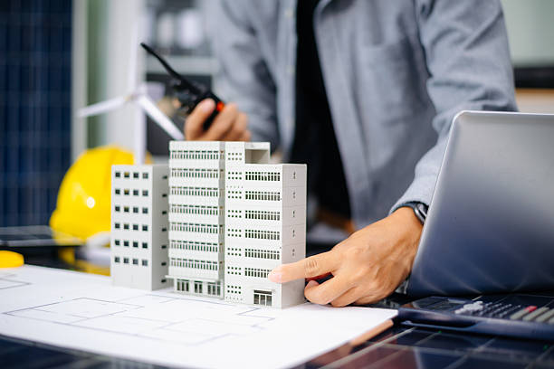 istock Engineer using compass on building plan with laptop, model, and wind turbine. Ideal for clean energy, architecture, 2233272039