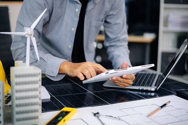 istock Engineer using compass on building plan with laptop, model, and wind turbine. Ideal for clean energy, architecture, 2233272040