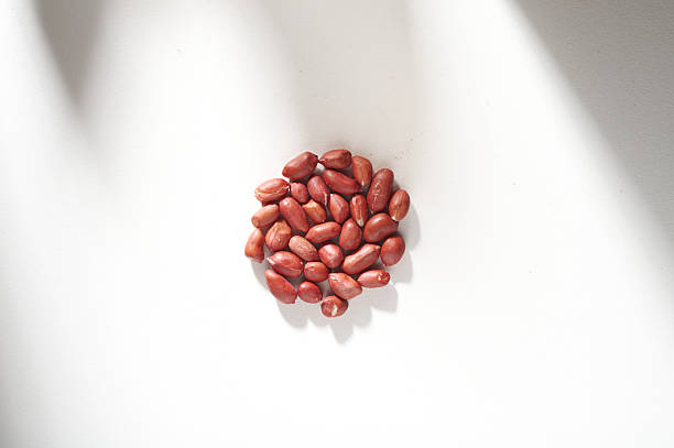 A Pile of Roasted Peanuts Scattered on a White Surface with Shadows
