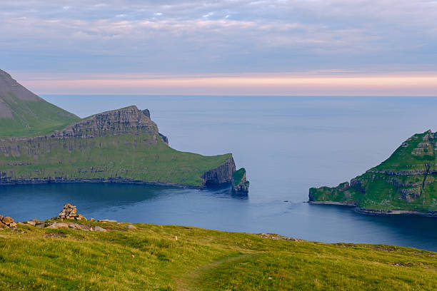 Vibrant green cliffs rise dramatically from the calm sea, creating a breathtaking landscape in the Faroe Islands during sunset. A serene view that captures natures beauty and tranquility.