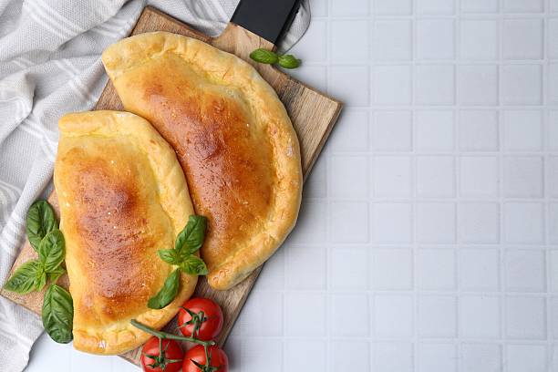 Tasty vegetarian calzones with basil and tomatoes on white tiled table, top view. Space for text