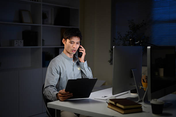 istock Adult businessman communicates on phone while checking paperwork at desk 2233286731