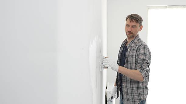 istock Construction worker wearing gloves and using a putty knife to plaster a white wall, performing home renovation and improvement tasks with precision 2233289662