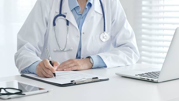 istock Female doctor documenting patient information while working with digital devices in a minimalist white workspace. Medicine and health care concept 2233294128