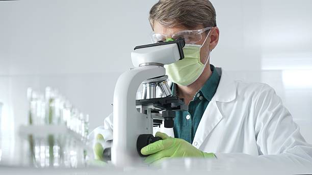 istock Adult male scientific professional analyzing sample through microscope, wearing green protective gear in sterile laboratory setting. Medicine, healthcare and science concept 2233297831