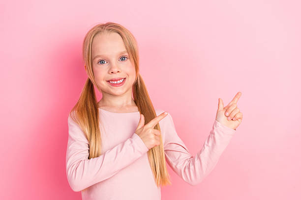 Bright scene of a smiling schoolgirl standing and gesturing with both hands on a lively pink background, full of youthful joy.