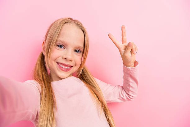 istock Cheerful young girl in pink showing a peace hand gesture while smiling happily against a vibrant pink background 2233298521