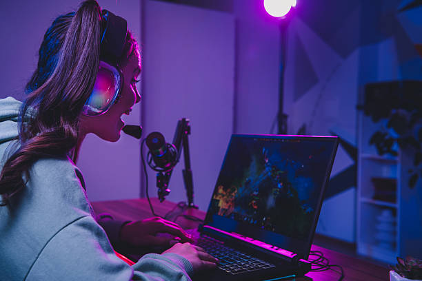 istock Young woman streaming video game online at home using professional setup with headset and microphone in cyber-inspired lighting 2233298642