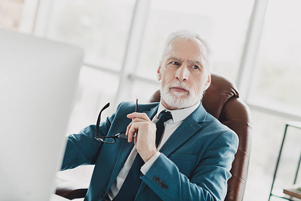 istock Professional senior businessman at office desk, holding glasses and deep in thought while working on business strategies 2233298896