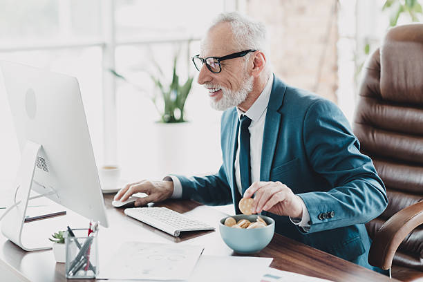 istock Senior businessman in formal suit smiling while working on a computer at his office desk during a coffee break 2233299007