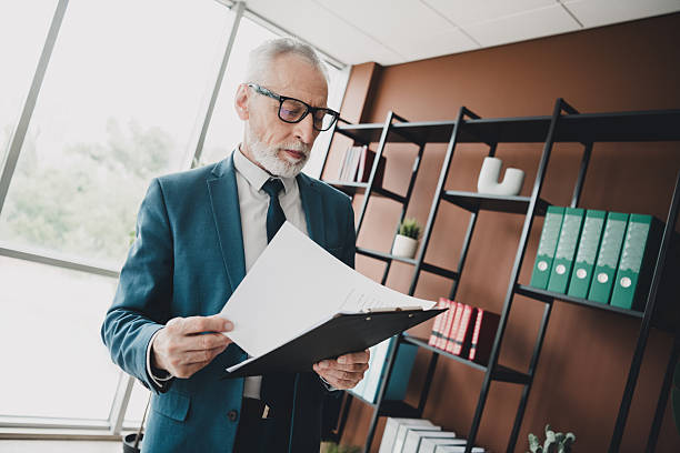 istock Confident senior businessman reviewing documents in modern office workspace with shelves and window light 2233299073