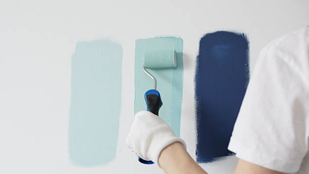 istock Painter wearing protective gloves rolling blue paint on white wall, creating gradient color effect for home interior renovation project 2233301194