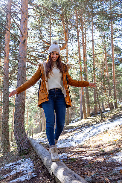 istock Young woman carefully balancing on fallen tree trunk in snowy forest 2233305919