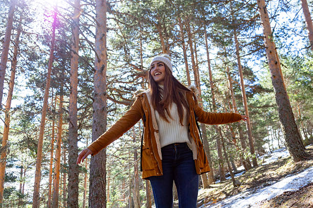 istock Young woman exploring a sunny winter forest with open arms 2233305924