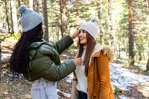 istock Two smiling young women fixing winter hats in snowy forest 2233305954