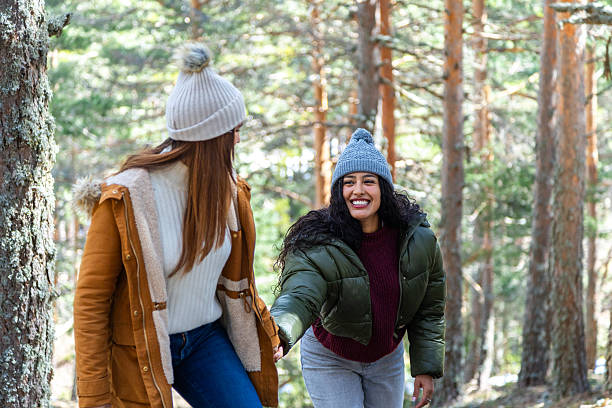 istock Two young women holding hands, smiling, and walking in winter forest 2233305957