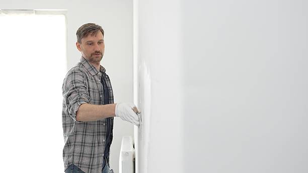 istock Construction worker wearing gloves and using a putty knife to plaster a white wall, performing home renovation and improvement tasks with precision 2233306525