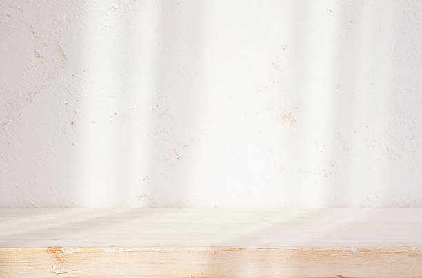 istock Bleached wood table top and abstract blurred plaster wall with shadows from window sunlight as background 2233306758