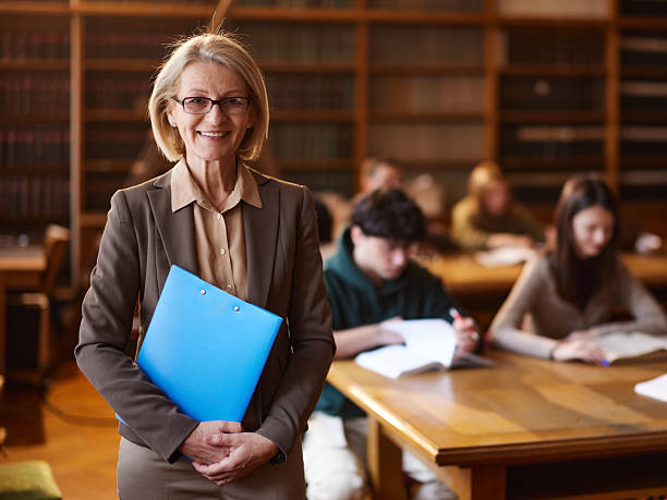 istock Happy mature professor with her students in library. 2233310418