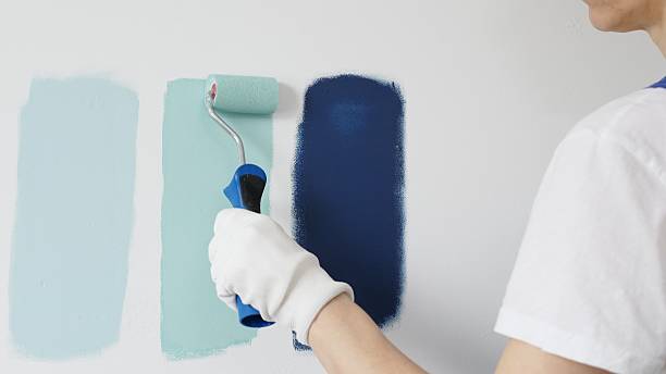 istock Painter wearing protective gloves rolling blue paint on white wall, creating gradient color effect for home interior renovation project 2233313701