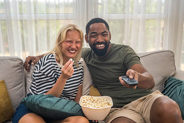 istock Young happy couple enjoying free time at home, sitting on sofa, watching television, eating popcorn, spending quality time together. Weekend activities of people in love. 2233317543