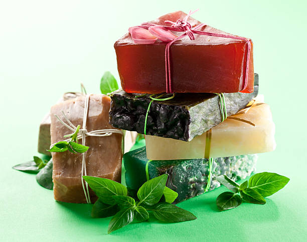 istock Stack of handcrafted natural soaps tied with rustic strings and green fresh herb leaves on light green background. 2233321700