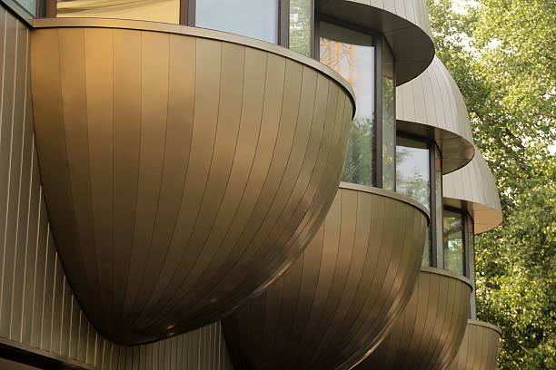 Modern architectural design featuring curved metallic balconies against a backdrop of green foliage.