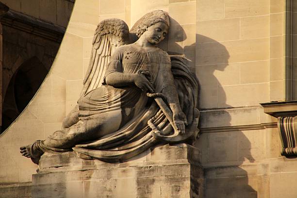 Stone angel sculpture on a historic building facade in Paris, France, with soft sunlight casting shadows.