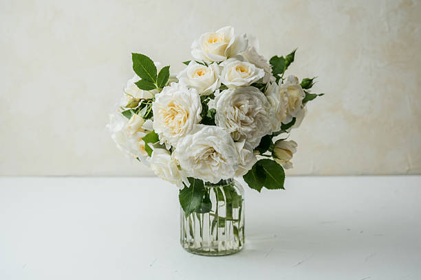 istock White roses bouquet in glass vase on white table with light background 2233324379