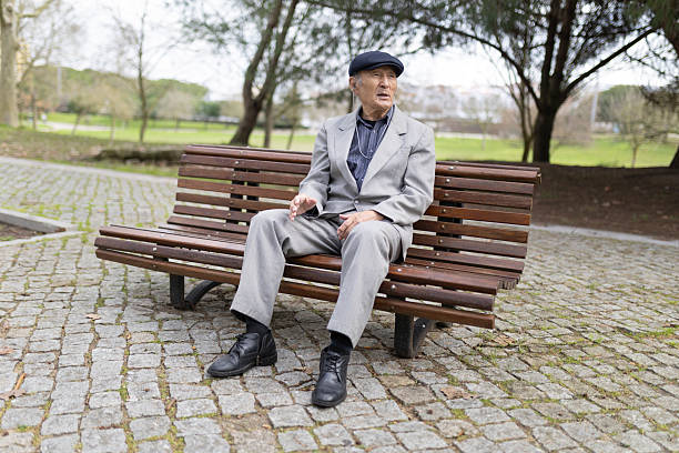 istock Elegant senior man sitting on bench in park talking and gesturing 2233326879