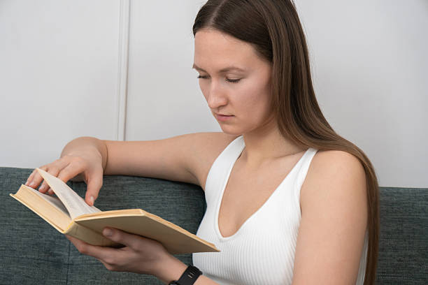 istock Young woman is reading a book at home, possibly a student studying a textbook, with a serious and focused expression, indicating deep concentration and engagement with the material 2233328345
