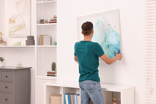 istock Decorator hanging abstract picture indoors, back view 2233328925