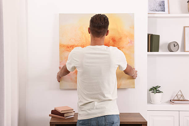 Male decorator hanging abstract picture indoors, back view