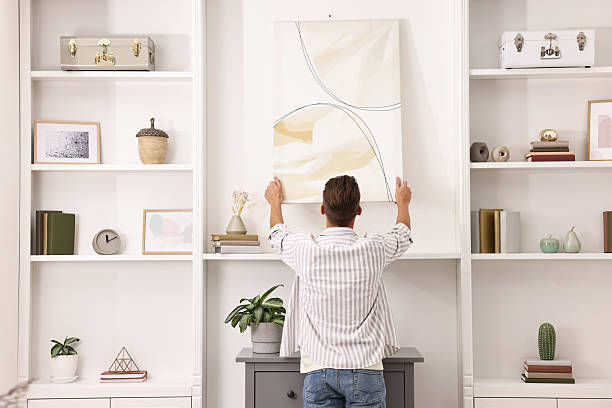 istock Male decorator hanging abstract picture indoors, back view 2233329028
