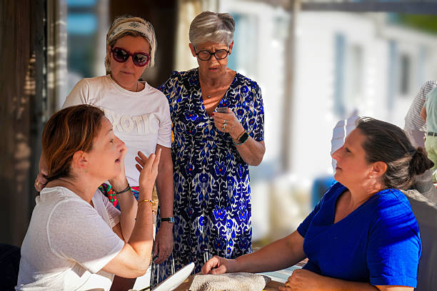 A group of four adults enjoying a lively outdoor conversation on a sunny day. Two are seated, actively engaging in storytelling and listening, while the other two stand nearby, attentively participating. The relaxed atmosphere, warm light, and casual attire suggest a seasonal gathering, highlighting authentic moments of connection and shared beauty tips among friends.