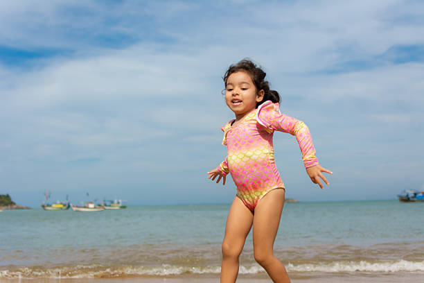 Little girl having fun in the sand at the beach. Jumping the waves with her bucket.