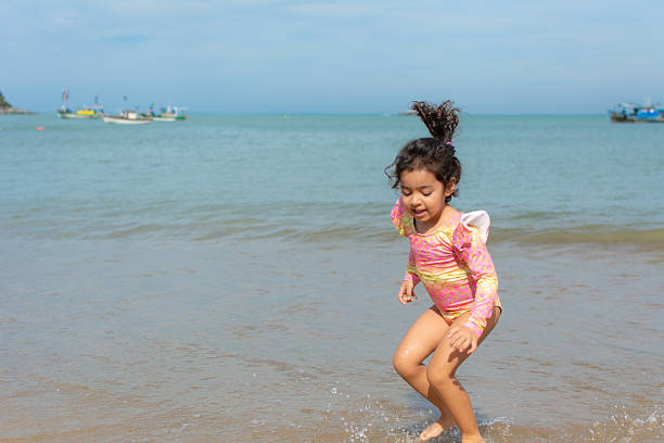 Little girl having fun in the sand at the beach. Jumping the waves with her bucket.
