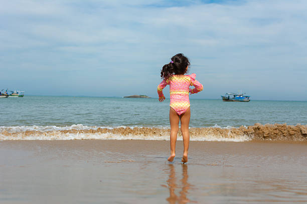 Little girl having fun in the sand at the beach. Jumping the waves with her bucket.