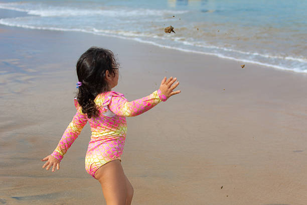 Little girl having fun in the sand at the beach. Jumping the waves with her bucket.