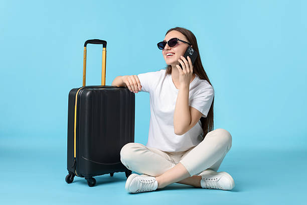 istock Woman with suitcase talking on smartphone against light blue background 2233344480