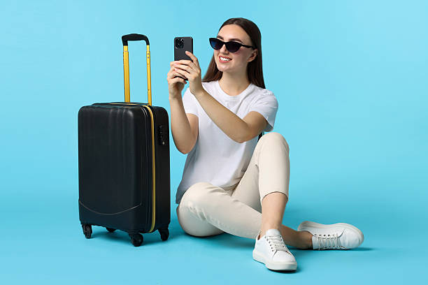 istock Woman with suitcase taking selfie on light blue background 2233344616
